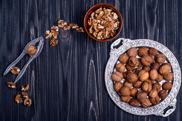 Fototapeta na wymiar Walnuts and walnut kernelsin a silver dish on a dark wooden background