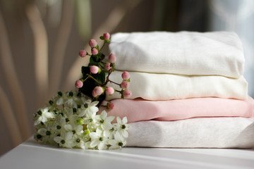 a stack of neatly folded women's clothing in light shades, decorated with white and pink flowers in sunlight