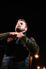 A man in a jumper and waistcoat posing on the street at night. Advertising of men's clothing