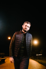 A man in a jumper and waistcoat posing on the street at night. Advertising of men's clothing