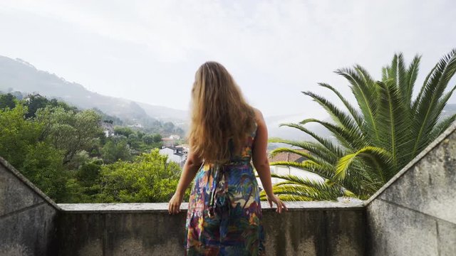 View through opened doors woman standing on balcony of traditional country house in valley of Douro river in winemaking region in Portugal. Girl touching hairs and enjoying beautiful panoram