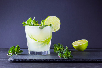 Cocktail mojito and mint on black background. Refreshing cocktail with lime and fresh mint on slate board. Summer drink with citrus and ice