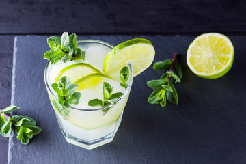 Cocktail mojito and mint on black background. Refreshing cocktail with lime and fresh mint on slate board. Summer drink with citrus and ice