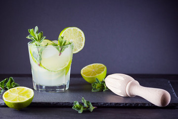 Cocktail mojito and mint on black boards. Refreshing cocktail with lime and fresh mint on slate board. Summer drink with citrus and ice. Manual wooden juicer and mojito