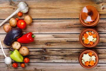 Traditional rustic home vegetable stew with raw vegetables and spices in clay pots on an old vintage wooden table.