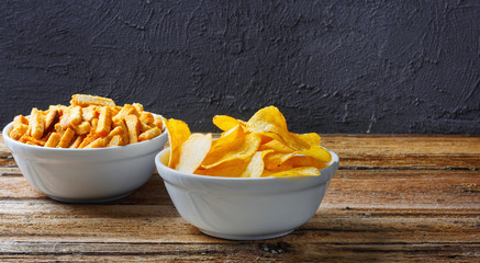 Chips, crackers in bowls on wooden table on brick wall
