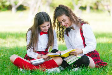 two schoolgirls in school uniforms sit with books in the park. Schoolgirls or students are taught lessons in nature