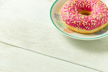 Donut on a plate and on a wooden table. Photo of sweets with copyspace.