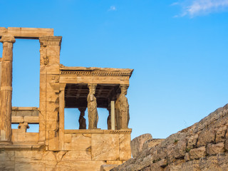 Fototapeta na wymiar Porch of Poseidon, part of Erechtheion, sacred olive tree, walls of temple of Athena Polias on Acropolis, Athens, Greece against blue sky