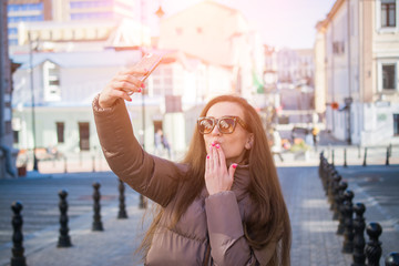 Fototapeta premium Beautiful young woman is blowing a air kiss while posing for a selfie