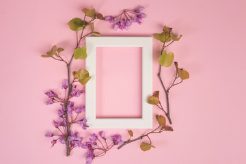 Flowers composition. Purple flowers, leaves and photo frame on pastel pink background. Flat lay, top view, copy space