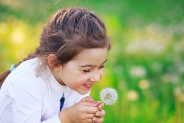 Beautiful little Girl blowing dandelion flower and smiling in summer park. Happy cute kid having...