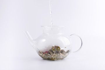 Pouring hot water to the glass teapot with herbal tea, isolated on white background