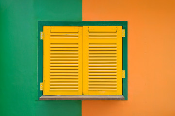 The old window with yellow shutters on a green orange wall. Vintage background.