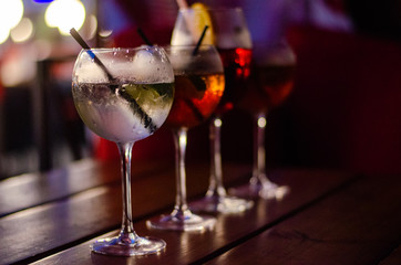 Beautiful row line of different colored alcohol cocktails on a party, martini, vodka,and others on decorated catering bouquet table on open air event, picture with beautiful bokeh