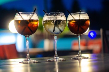 Beautiful row line of different colored alcohol cocktails on a party, martini, vodka,and others on decorated catering bouquet table on open air event, picture with beautiful bokeh