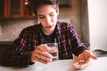 young man has a terriuble headache in the motning and hold a glass with water