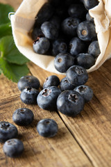 Blueberries spilling out of a brown textile, eco bag over rustic wood table. Zero waist concept, no plastic. Eco friendly berries, fruits. Bio berry.