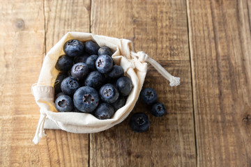 Zero waist concept, no plastic. Blueberries spilling out of a brown textile, eco bag over rustic wood table. Eco friendly berries, fruits. Bio berry.