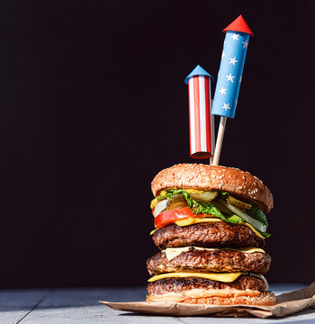 A Big Burger With Three Juicy Beef Patties Bonded With American Flag Firework Skewers. Burgar Concept For The Day Of Independence Day Celebration Of Fourth Of July