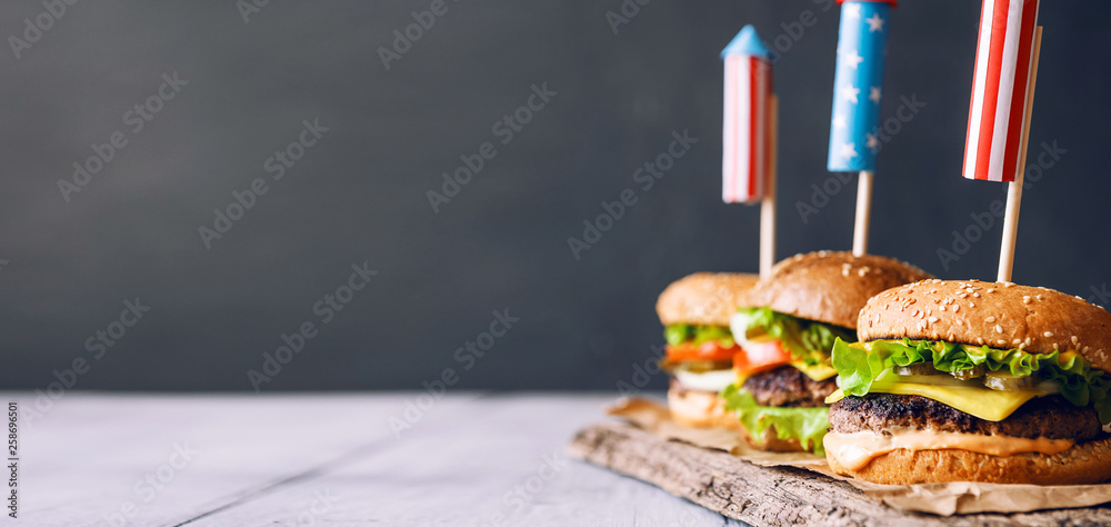 Wall mural three fresh and juicy burgers with American flag-style fireworks inserted into them. bbq concept picnic to celebrate independence day