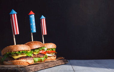 three fresh and juicy burgers with American flag-style fireworks inserted into them. bbq concept picnic to celebrate independence day