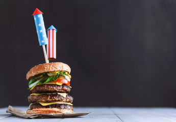 a big burger with three juicy beef patties bonded with American flag firework skewers. burgar concept for the day of independence day celebration of fourth of july - obrazy, fototapety, plakaty