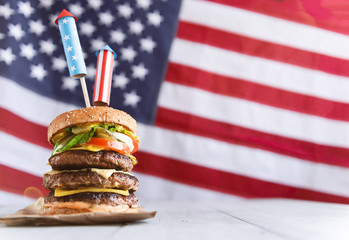 a big burger with three juicy beef patties bonded with American flag firework skewers. burgar concept for the day of independence day celebration of fourth of july - obrazy, fototapety, plakaty