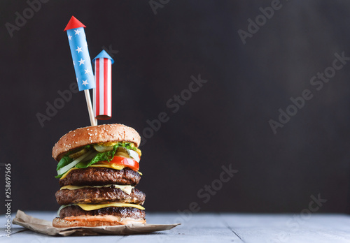 a big burger with three juicy beef patties bonded with American flag firework skewers. burgar concept for the day of independence day celebration of fourth of july