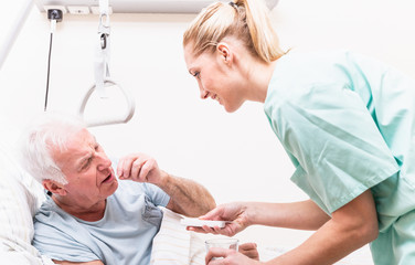 Junge Krankenfpflegerin gibt altem Mann Medikamente im Pflegeheim 