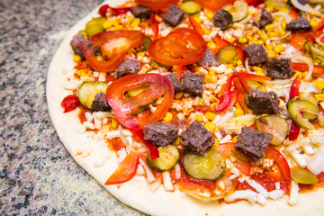Raw pizza on thin dough with tomatoes, beef, pickled cucumber, corn and red pepper
