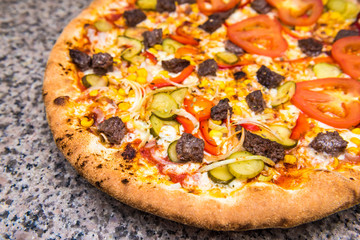 Fresh pizza on thin dough with tomatoes, beef, pickled cucumber, corn and red pepper