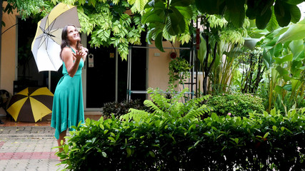 Young pretty woman in green dress walks in the rain. Hand of women holding an umbrella.