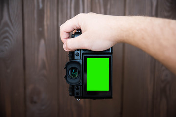 Hand holding and taking shot with green display mirrorless camera on wooden table