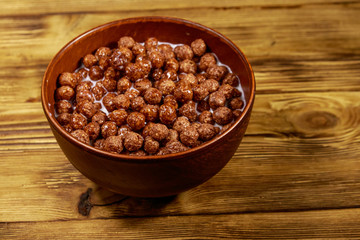 Cereal chocolate balls with milk in a bowl on wooden table