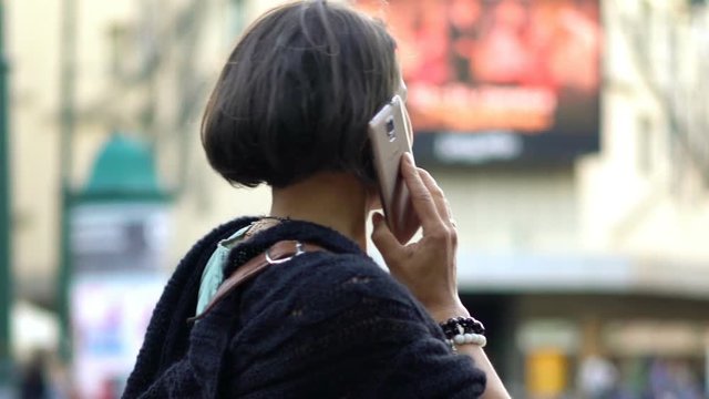 Happy, young woman talking on cellphone in city