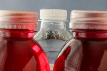 Plastic bottle with red colored drink and focus on clear water in plastic bottle in back