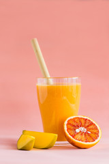 Mango and orange smoothie in glass on pink background.