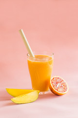 Mango and orange smoothie in glass on pink background.
