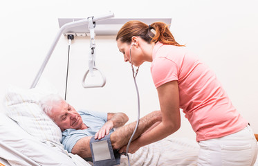 Junge Pflegerin mit altem Menschen Mann im Pflegeheim bei der Pflege Blutdruck messen 