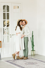 Young beautiful pregnant woman and her husband in hat standing near cactus wall