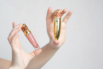 Female hand holding lip gloss and lipstick in a designer packaging over a grey background. Empty space
