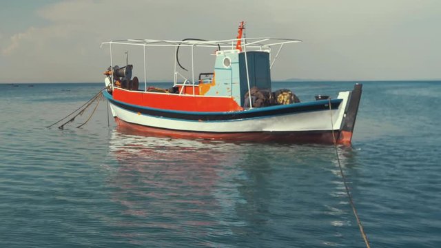 Traditional carvel built Greek fishing boat moored at sea RAMPED SLOW MO, pan up.