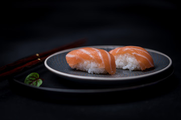 salmon sushi on dark plate with chopsticks and soy sauce
