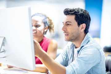 Two young colleagues in smart casual wear discussing something while spending time in the office,African girls learn to work from handsome man by computer