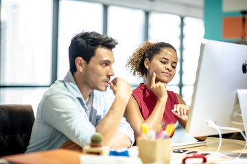 Two young colleagues in smart casual wear discussing something while spending time in the office,African girls learn to work from handsome man by computer
