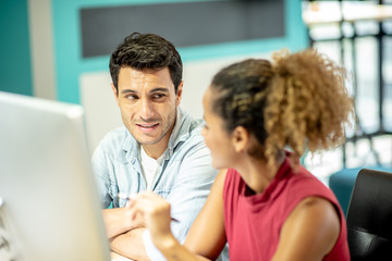 Two young colleagues in smart casual wear discussing something while spending time in the office,African girls learn to work from handsome man by computer