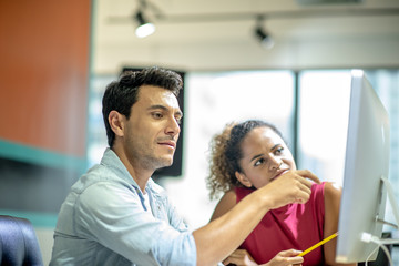 Two young colleagues in smart casual wear discussing something while spending time in the office,African girls learn to work from handsome man by computer