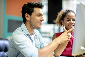 Two young colleagues in smart casual wear discussing something while spending time in the office,African girls learn to work from handsome man by computer