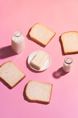 Butter on ceramic plate surrounded by bread and milk on pink background